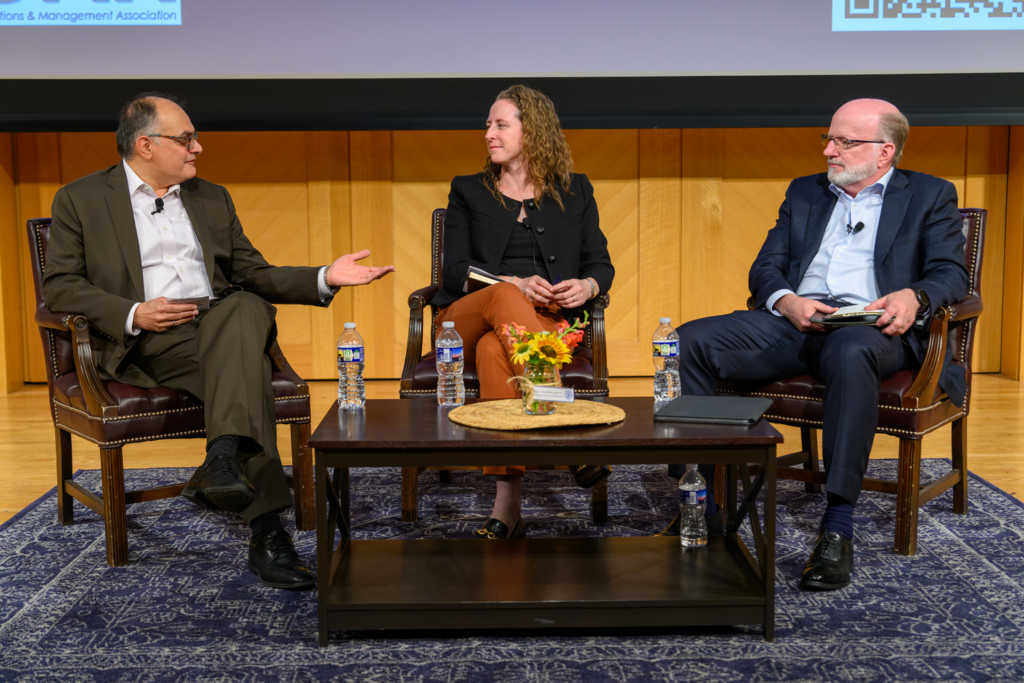 Three professionals sit on stage having an engaged conversation. 